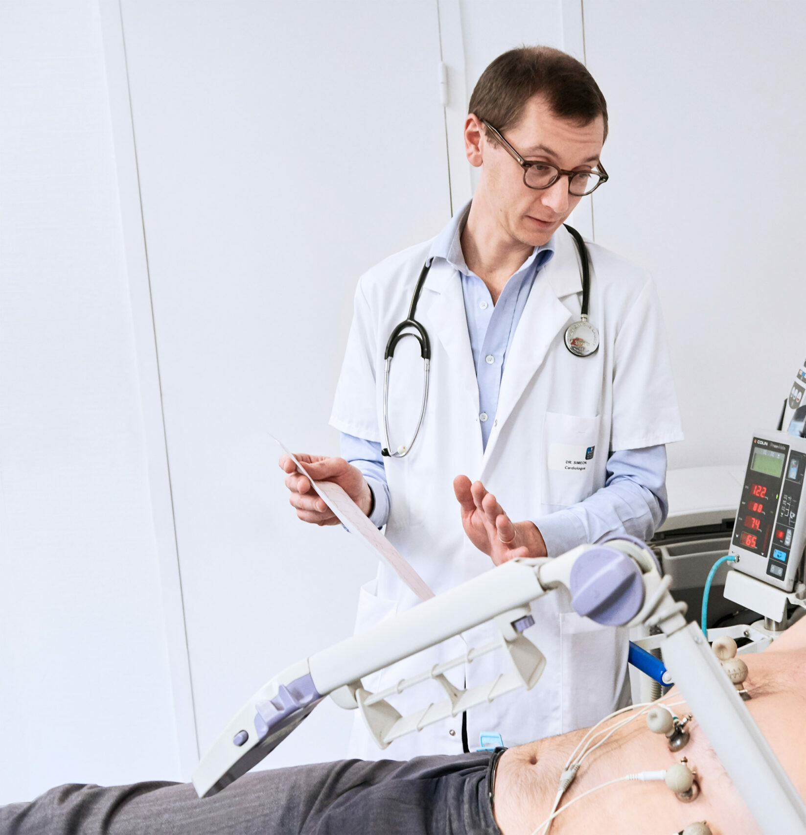 Médecin analysant un électrocardiogramme en temps réel chez un patient allongé – examen standard pour détecter une anomalie du rythme cardiaque